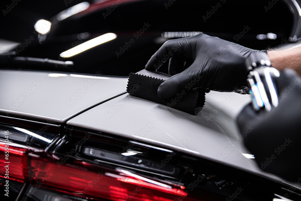 Employee of a car detailing studio or car wash applies a ceramic coating to the paint of a gray car