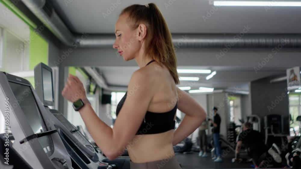 A young woman in a gym runs on a treadmill. A confident girl athlete gains excellent physical shape and prepares for sports competitions. The concentration on achieving the perfect result for the A young woman in a gym runs on a treadmill. A confident girl athlete gains excellent physical shape and prepares for sports competitions. The concentration on achieving the perfect result for the