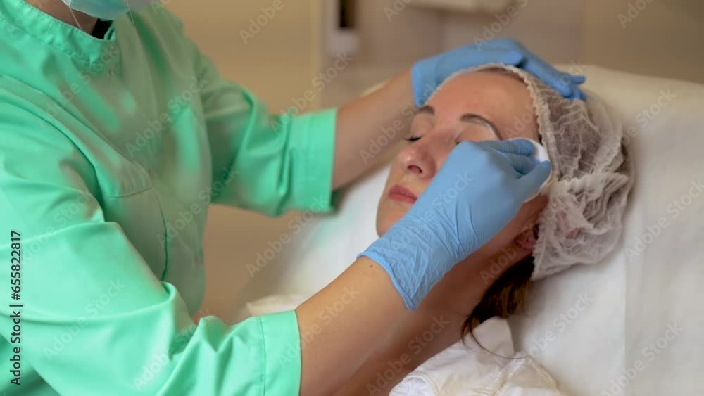 Doctor cosmetologist preparing cleaning face of Middle aged woman for neurotoxin acid anti aging injection. Anti aging injections with syringe, cosmetology in clinic salon for client Doctor cosmetologist preparing cleaning face of Middle aged woman for neurotoxin acid anti aging injection. Anti aging injections with syringe, cosmetology in clinic salon for client