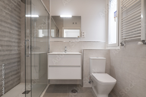 A small bathroom with a white towel radiator  a white wooden hanging cabinet with a sink and a frameless mirror on the wall.