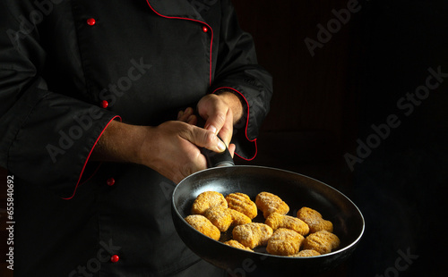 Experienced chef frying chicken nuggets in a frying pan. The concept of cooking nagits in the kitchen. Free space for advertising on a black background photo