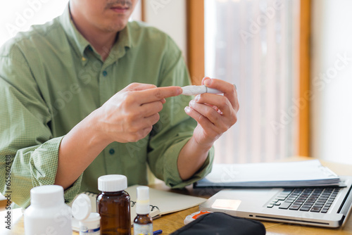 Close up of man hands using lancet on finger at home to check blood sugar level. Cropped hands of glaucometer while examining blood sugar test at home.