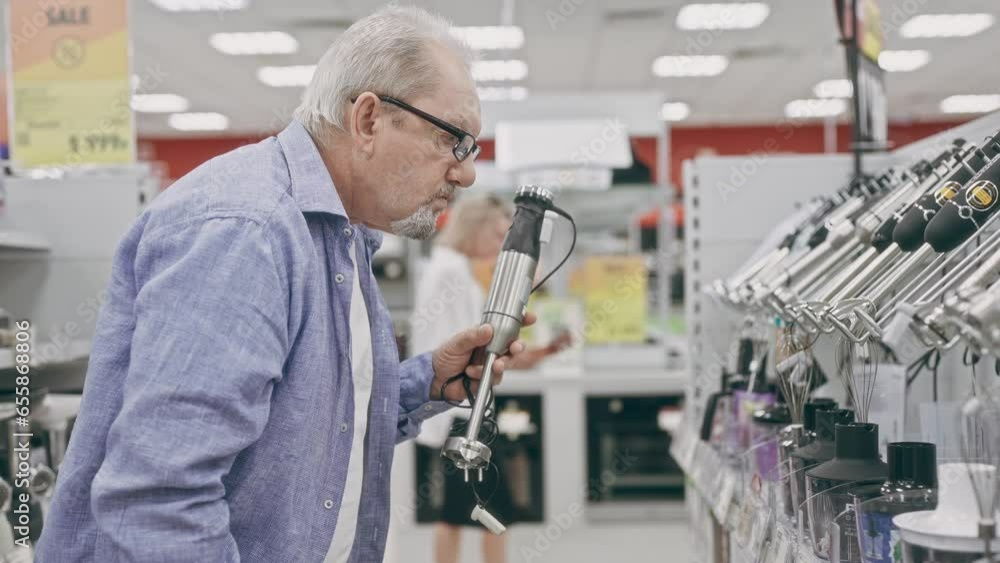 An elderly man in an electronics hypermarket chooses a blender. A pensioner chooses household appliances in a shop An elderly man in an electronics hypermarket chooses a blender. A pensioner chooses household appliances in a shop