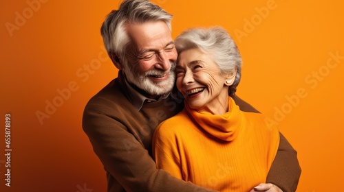 Un couple de personnes âgées de 70 ans s'enlaçant, seniors heureux, complice, arrière-plan coloré orange.