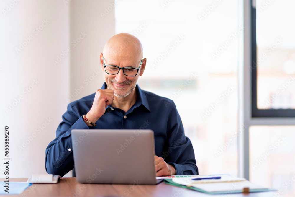 Shot of a mid aged businessman using a laptop in a modern office and having web conference Shot of a mid aged businessman using a laptop in a modern office and having web conference