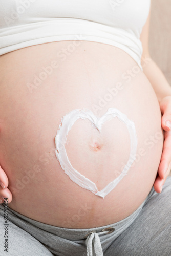 Wallpaper Mural a pregnant girl sits at home on the bed and smears heart an anti-stretch mark cream on her stomach. Pregnancy, motherhood, preparation and expectation concept Torontodigital.ca