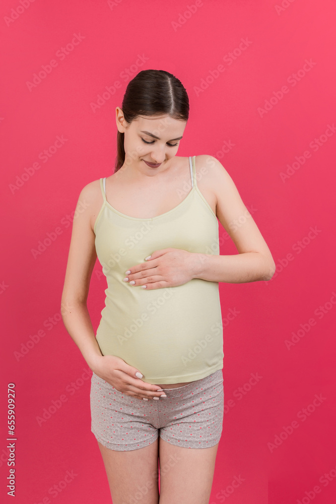 Happy pregnant woman touching her abdomen at Colored background. Future mother. Expecting of a baby. Copy space Happy pregnant woman touching her abdomen at Colored background. Future mother. Expecting of a baby. Copy space