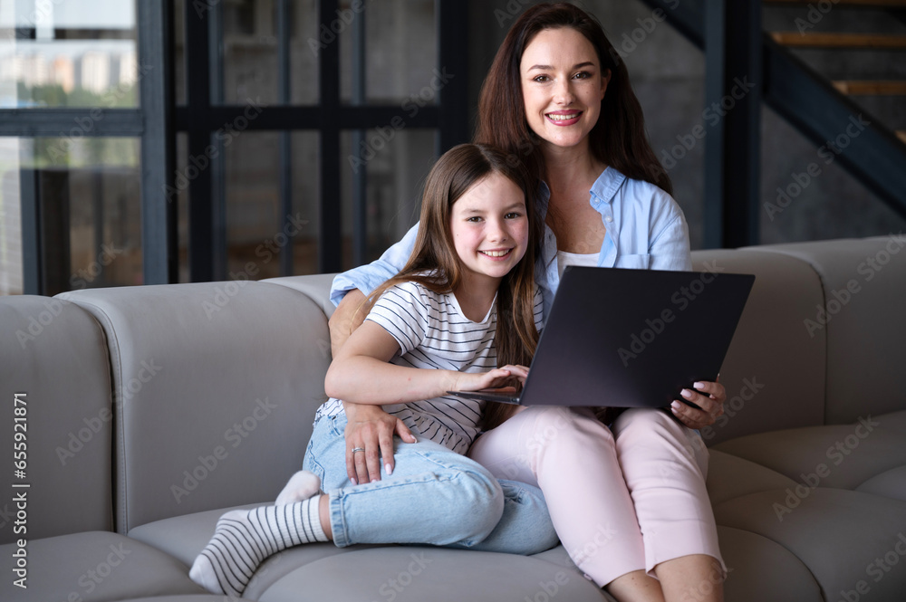 Woman with daughter sitting on couch and watching movie on laptop together Woman with daughter sitting on couch and watching movie on laptop together