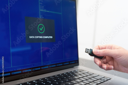 a person holding a usb device in front of a laptop. USB flash drive and laptop