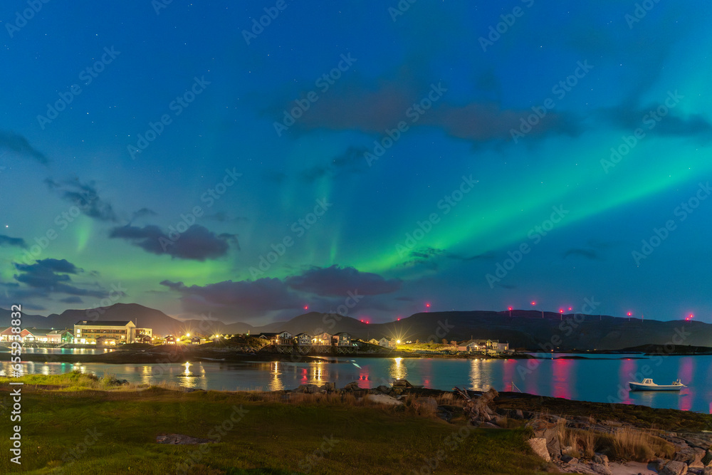 wonderful northern lights over the village of Hillesøya. strong contrast from dark sky with the green Aurora Borealis rising over the clouds, mirroring on fjord, Norway with dancing lady