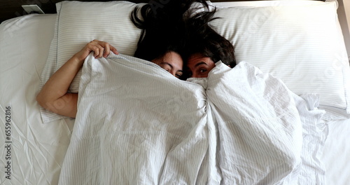 Fun loving young married couple hiding under blanket in bed, top view photo
