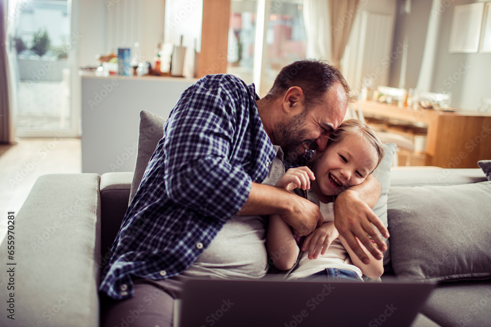 Happy young caucasian father and daughter using a laptop on the couch at home Happy young caucasian father and daughter using a laptop on the couch at home