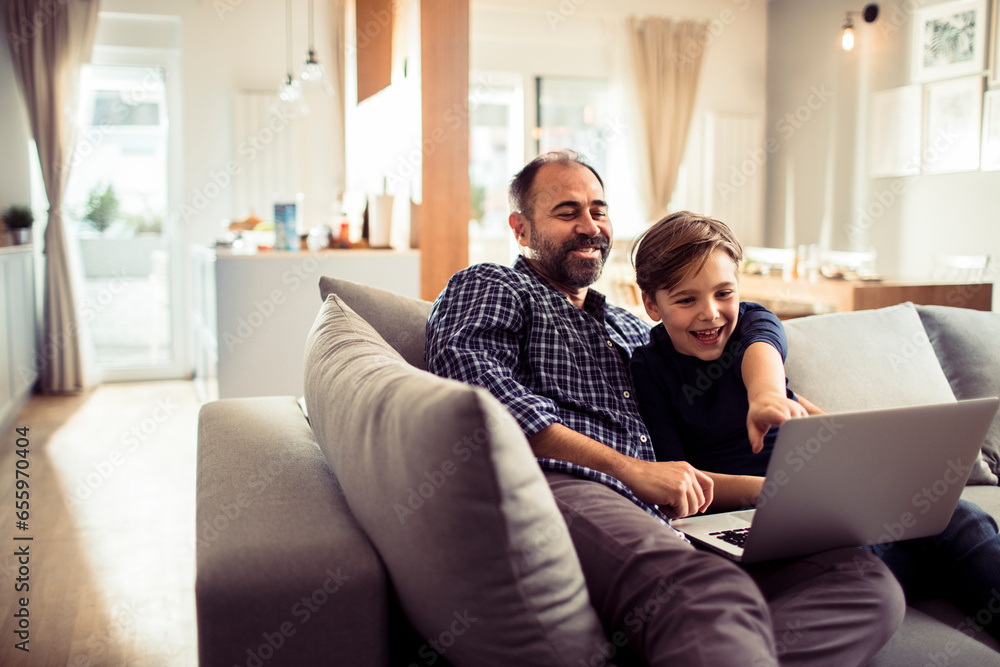 Happy young caucasian father and son using a laptop on the couch at home