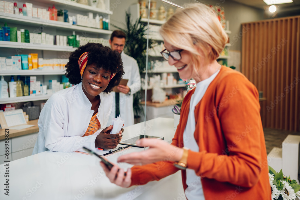 Obraz premium African american woman pharmacist selling drugs to a senior customer in a pharmacy