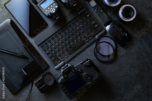 Equipo fotográfico profesional. Estación de trabajo de fotografía digital sobre fondo negro. Vista superior de cámara digital, flash, lente y computadora portátil.