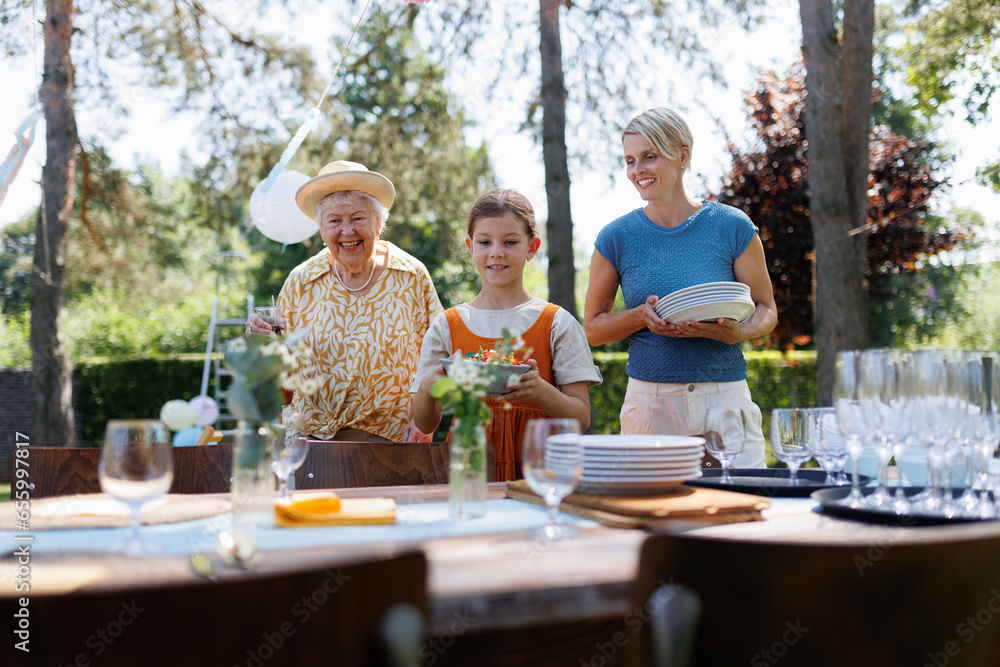 Grandmother, mother and daughter setting table for summer garden party. Grandmother, mother and daughter setting table for summer garden party.