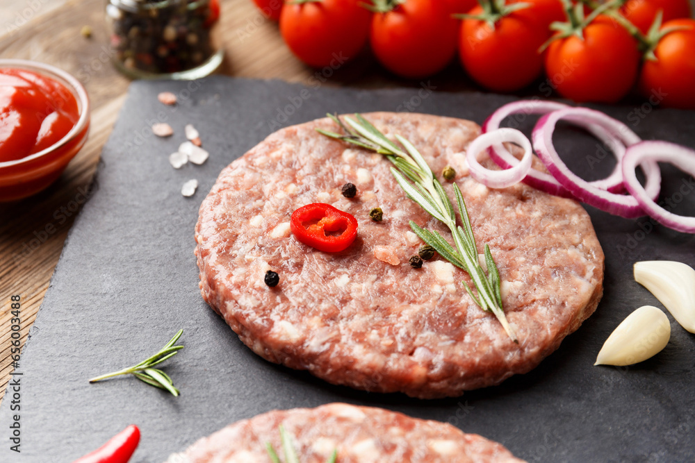 Raw beef hamburger patties on stone plate, vegetables and spices, wooden background. Raw beef hamburger patties on stone plate, vegetables and spices, wooden background.
