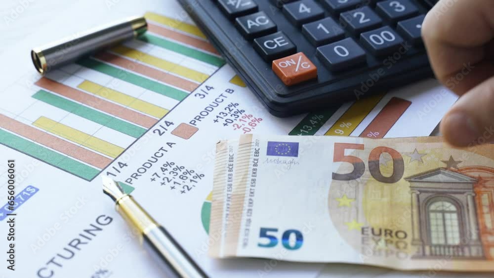 A man counts 50 euro bills and places them on the table next to business charts and a calculator. Business and finance concept. A man counts 50 euro bills and places them on the table next to business charts and a calculator. Business and finance concept.