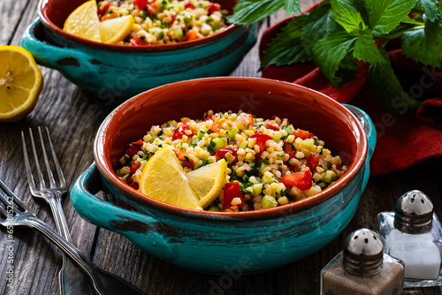 Tabbouleh salad -  bulgur groats, tomatoes, cucumber, parsley, lemon, onion and fresh mint leaves on wooden background
 photo