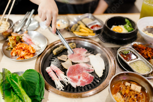 A woman's hand uses silver chopsticks to grill Korean-style pork.