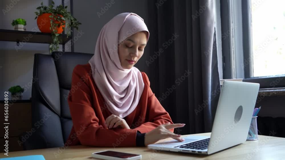 Medium-sized video capturing an attractive young woman wearing a hijab, veil. She is working on a laptop and casually talking on the phone, smiling. Medium-sized video capturing an attractive young woman wearing a hijab, veil. She is working on a laptop and casually talking on the phone, smiling.