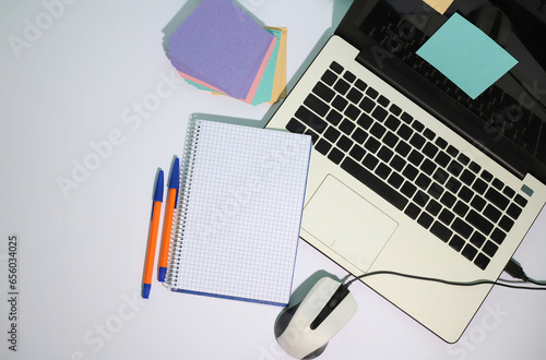 on a white background, a white laptop, a white computer mouse, a notepad, pens and multi-colored stickers for notes