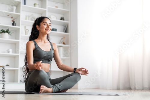 Happy young indian woman sitting in lotus pose at home photo