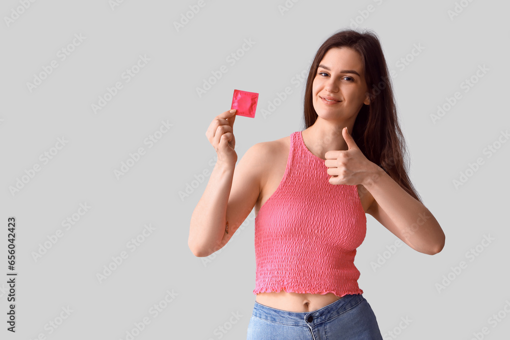 Young woman with condom showing thumb-up on light background Young woman with condom showing thumb-up on light background