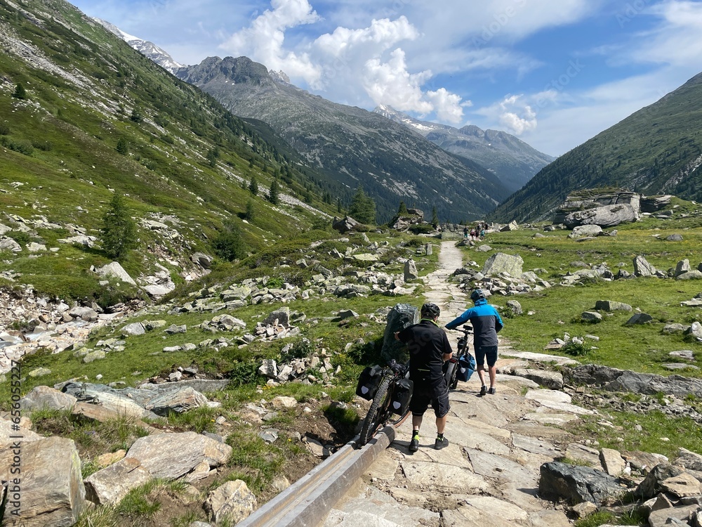 Fototapeta premium Mountainbiker schieben ihr Fahrrad bergab in den Zillertaler Alpen in der Nähe vom Pfitscherjoch in Österreich