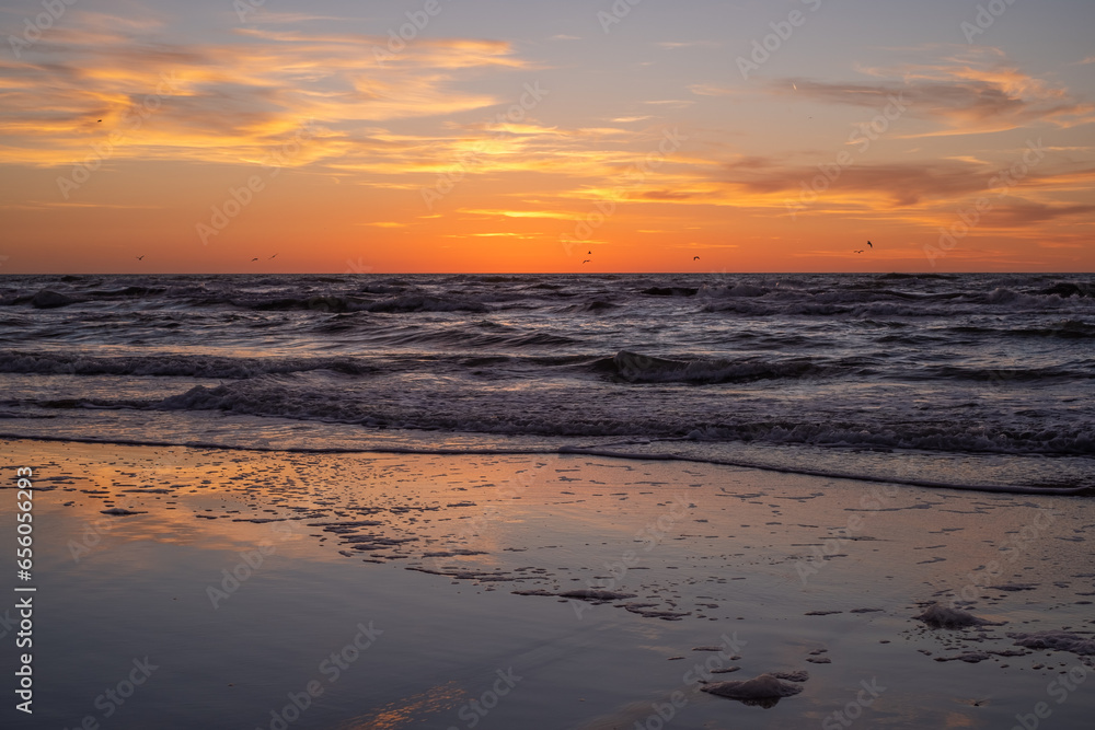 A peaceful, meditative sunset, white waves in the sea and orange-yellow clouds