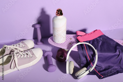 Composition with different sports equipment, shoes and bottle of water on lilac background