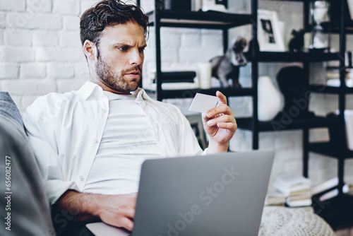 serious hipster guy confused with credit card number making transaction on netbook