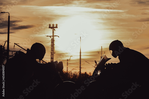 silhouettes of two people sitting on motorcycles facing each other at sunset