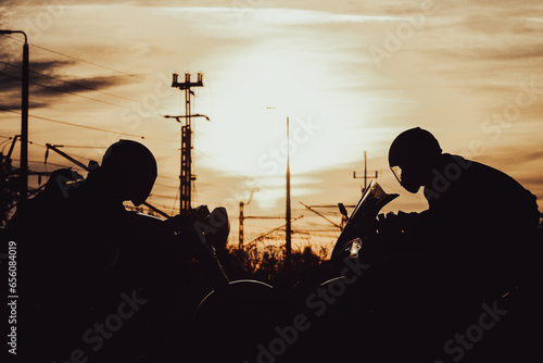 silhouettes of two people sitting on motorcycles facing each other at sunset