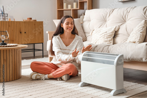 Young woman warming near radiator at home