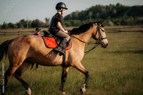 A teenage boy in a helmet learns horse riding in the summer, the instructor teaches the child equestrianism. © sushytska