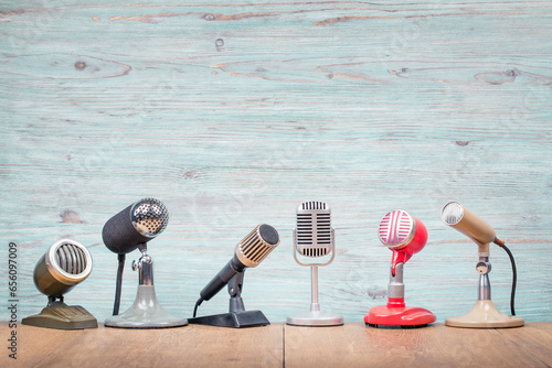 Retro old microphones for press conference or interview on table front textured light blue wooden wall background. Vintage old style filtered photo