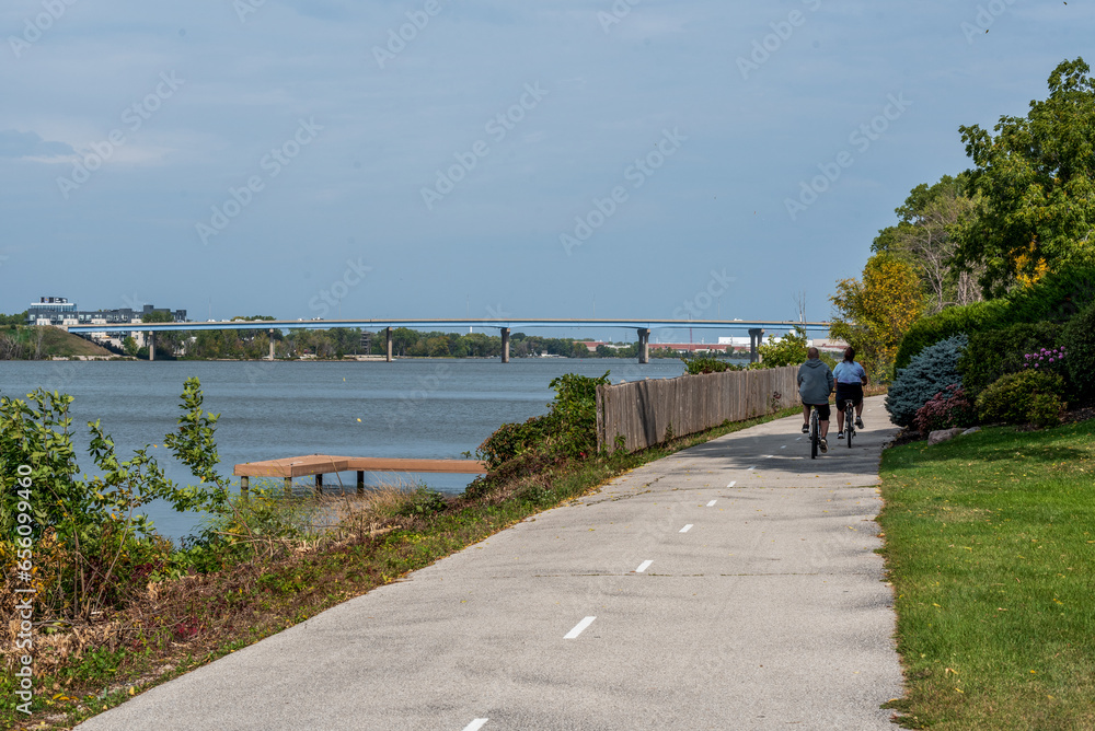 Bicycle Riders On The Fox River Trail Near De Pere, Wisconsin, With The Wisconsin 172 Bridge In The Distance