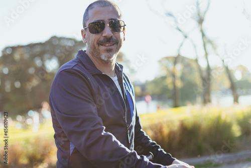42-year-old man with gray hair, beard, sunglasses, smiling in a plaza