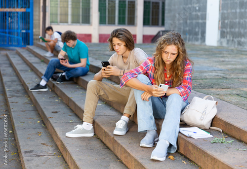 Girl and boy write messages on smartphone on city street