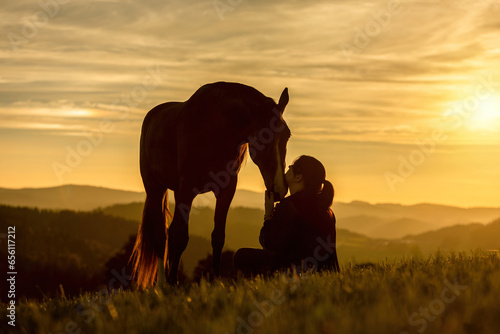 A young female equestrian and her arab berber horsein front of a romantic sunset landscape. Bond between a woman and her horse