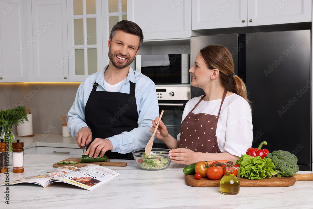 Happy couple reading recipe in culinary magazine while cooking at home Happy couple reading recipe in culinary magazine while cooking at home