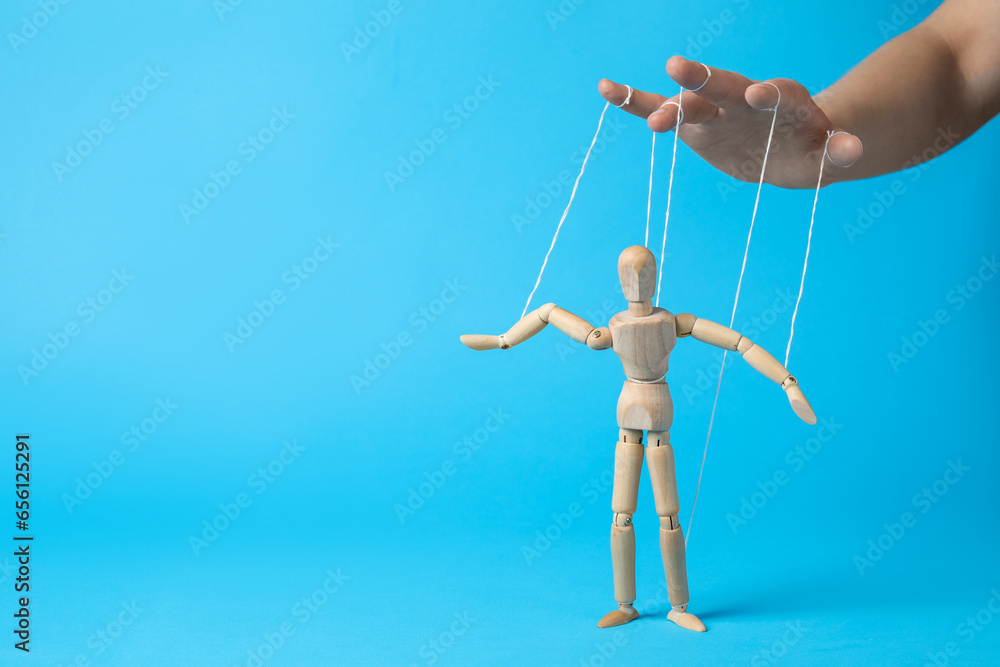Woman pulling strings of puppet on light blue background, closeup. Space for text