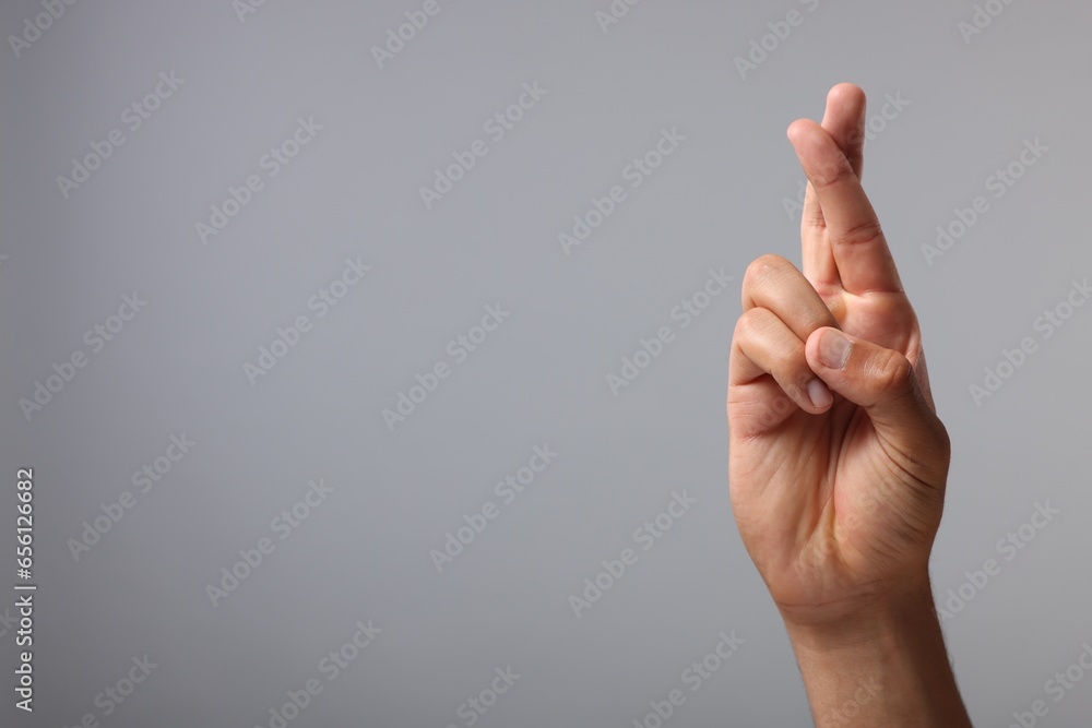 Man crossing his fingers on grey background, closeup. Space for text Man crossing his fingers on grey background, closeup. Space for text