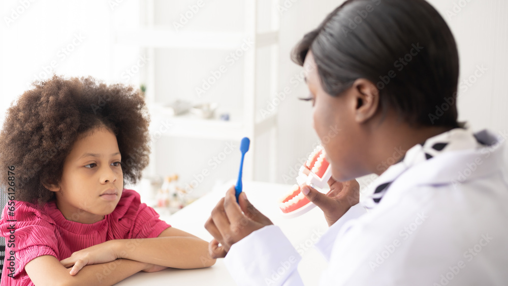 African American dentist explaining to mixed-race afro child how to brush teeth. The doctor and healthcare concept for children. African American dentist explaining to mixed-race afro child how to brush teeth. The doctor and healthcare concept for children.