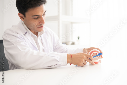 Hispanic dentist explaining to patient about teeth and how to brush with dental teeth model. The clinic treatment and healthcare concept with copy space background.