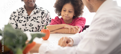 Hispanic nutritionist doctor consulting mixed-race child with her African American mother about a nutrition. Vegetables food - a new way for the good healthy and lifestyle.