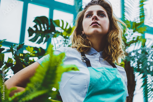 contemplative caucasian woman in casual apron looking away in warmhouse photo