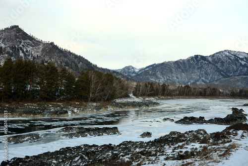 Rocky formations in the bed of a frozen river in a mountain valley covered with snow on a cloudy winter morning.
