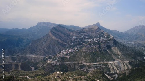 Aerial view mountain summit serpentine gravel road admiring authentic hillside village landscape rocky slopes. Drone shot contemplating gorgeous suburb summer countryside town on cliff rock 4k 4
